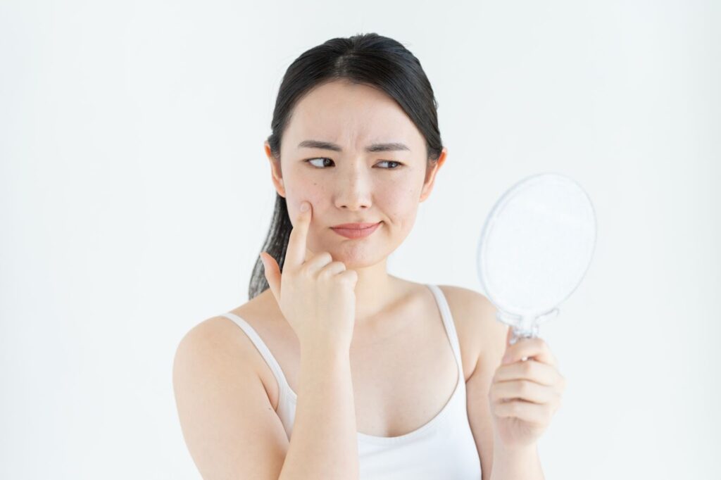 頬を指で触りながら鏡を見る女性