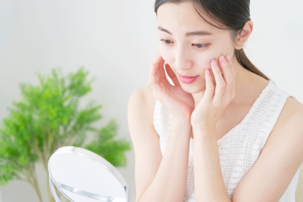 両頬に手を添えながら鏡で自分の顔を見る女性