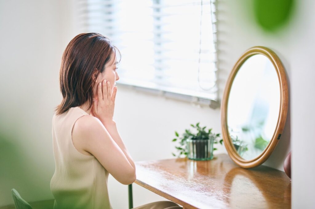鏡を見ながら頬を押さえる女性