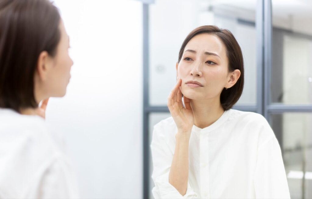 鏡で自分の顔を見ながら悩む女性